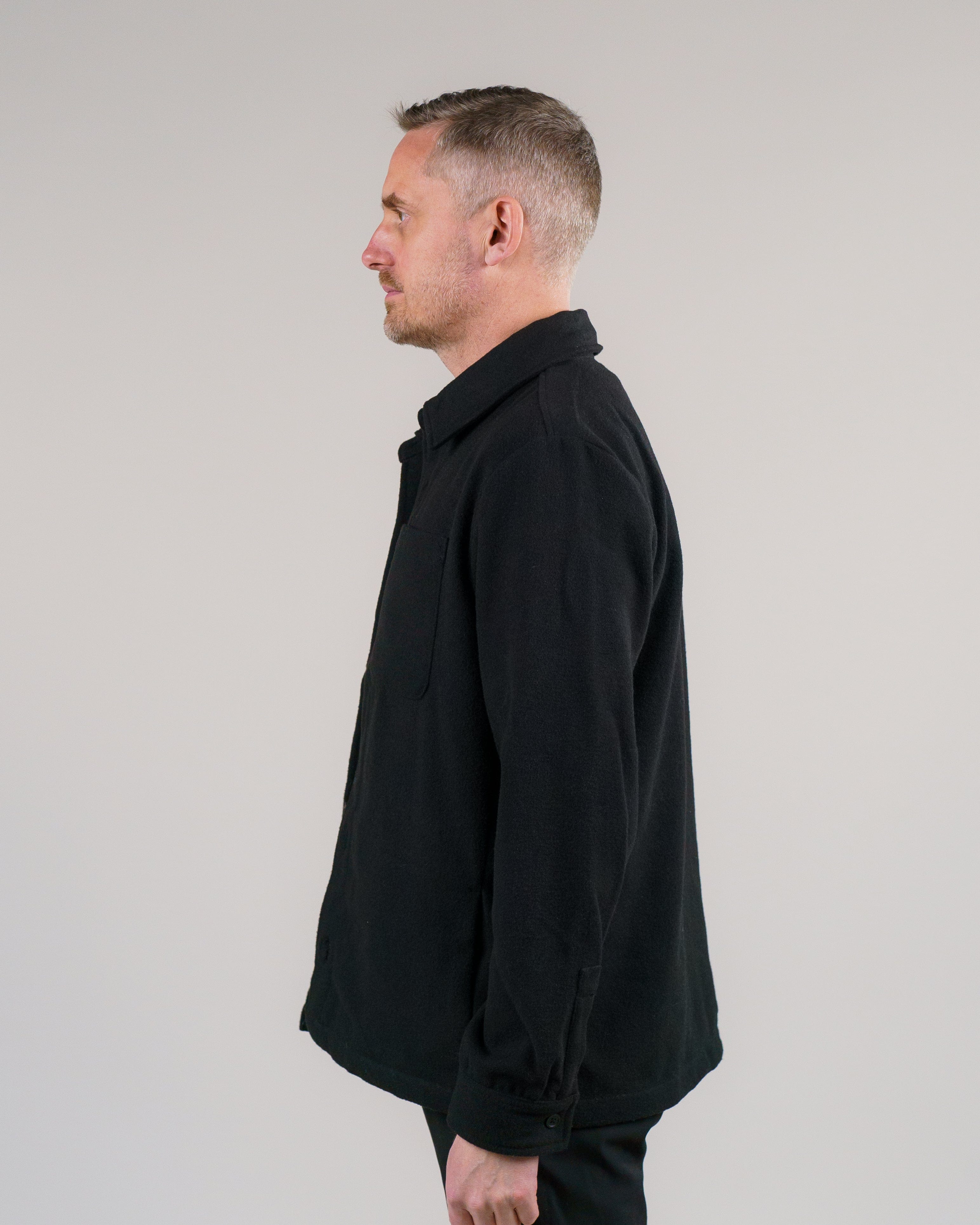 En mand iført en sort overshirt står i profil mod en neutral baggrund.